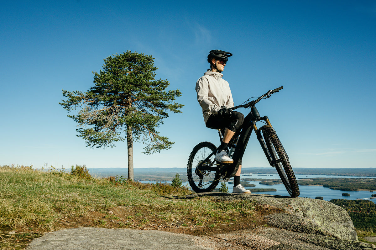 Cyclist resting on an e-mountain bike on a hilltop above lakes and forest — FANS